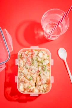 Plastic container with Russian salad and plastic utensils with red background Stock Photos