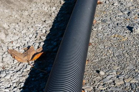 Plastic corrugated black pipe lying on a rocky surface. Stock Photos