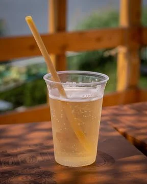 A plastic cup of apple cider with a biodegradable straw,  on a wooden table. Stock Photos
