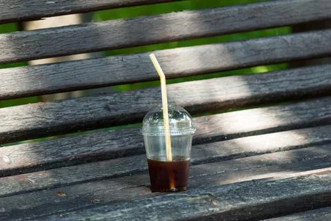 Plastic cup with leftover iced coffee on an old wooden park bench Stock Photos