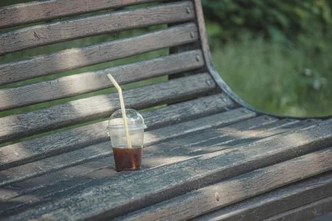 Plastic cup with leftover iced coffee on an old wooden park bench Stock Photos