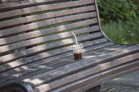 Plastic cup with leftover iced coffee on an old wooden park bench Stock Photos