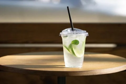 Plastic cup with lime and mint drink on wooden table in sunlight Stock Photos