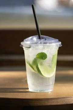 Plastic cup with lime and mint drink on wooden table in sunlight Stock Photos