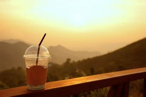 Plastic cup with straw on  mountain layers background during sunset Stock Photos