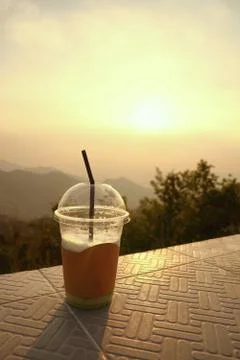 Plastic cup with straw on  mountain layers background during sunset Stock Photos