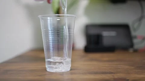 Plastic Cup on Wooden Kitchen Table Filling with Thin Water Stream from Another Stock Footage 321528432
