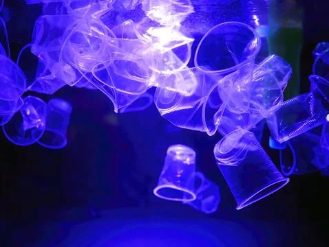 Plastic cups and bottles garbage drifting in an illuminated blue lights wat.. 스톡 사진