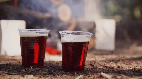 Plastic cups with cool drink are standing near burning fire on picnic in woods Stock Footage 91396580