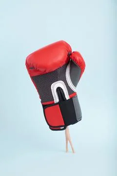 Plastic doll legs in heavy staggering boxing glove on minimal blue background Stock Photos
