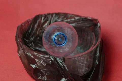 Plastic empty bottle in a black bag in container on red background. Concept o Stock Photos