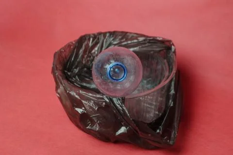 Plastic empty bottle in a black bag in container on red background. Concept o Stock Photos