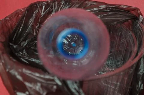 Plastic empty bottle in a black bag in container on red background. Concept o Stock Photos