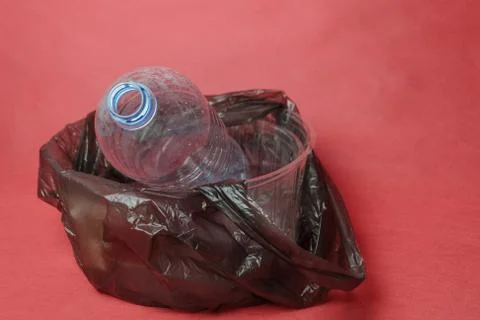 Plastic empty bottle in a black bag in container on red background. Concept o Stock Photos