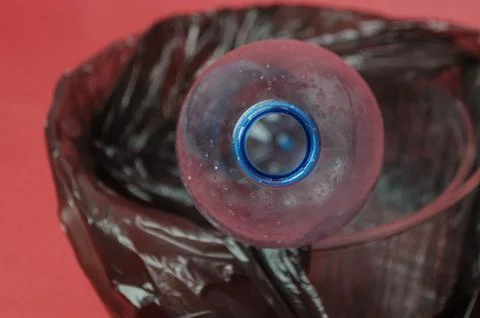 Plastic empty bottle in a black bag in container on red background. Concept o Stock Photos