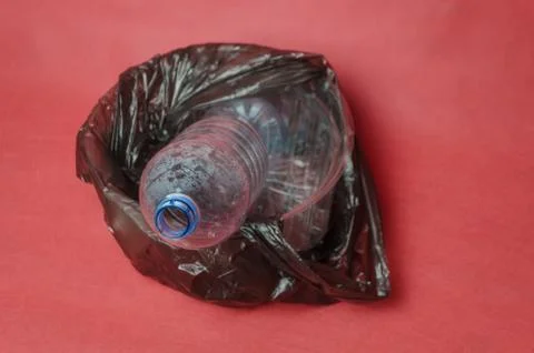 Plastic empty bottle in a black bag in container on red background. Concept o Stock Photos