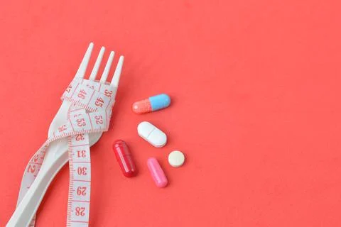 Plastic fork, pill capsules and measuring tape over red background. Stock Photos