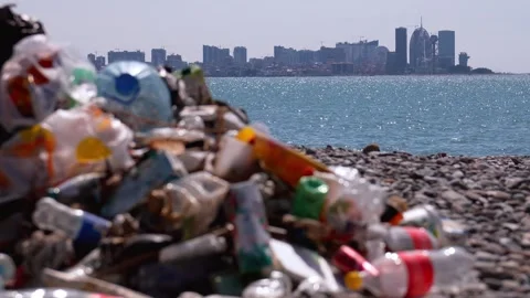Plastic garbage polluting a pebble beach with a city skyline 库存影片 338161634
