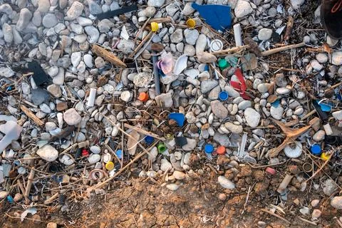 Plastic garbage on the seashore. Top view of a polluted beach. Stones and shells Stock Photos
