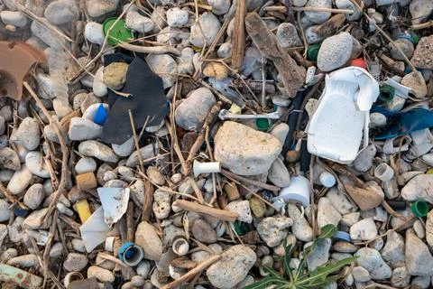 Plastic garbage on the seashore. Top view of a polluted beach. Stones and shells Stock Photos