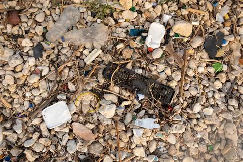 Plastic garbage on the seashore. Top view of a polluted beach. Stones and shells Stock Photos