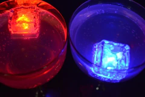 Plastic ice cubes with LEDs float in drinks of red, blue, green light. Stock Photos