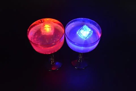 Plastic ice cubes with LEDs float in drinks of red, blue, green light. Stock Photos