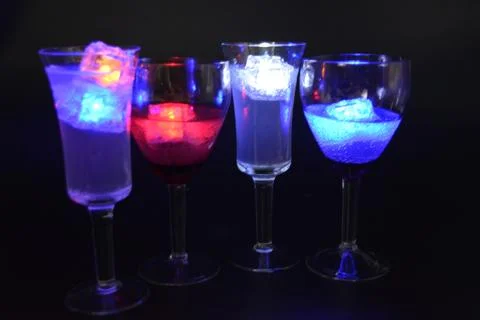 Plastic ice cubes with LEDs float in drinks of red, blue, green light. Stock Photos