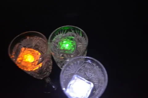 Plastic ice cubes with LEDs float in drinks of red, blue, green light. Stock Photos