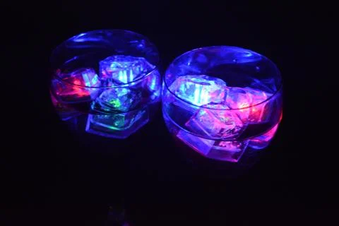 Plastic ice cubes with LEDs float in drinks of red, blue, green light. Stock Photos