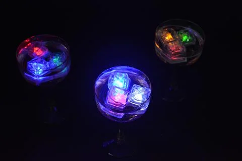 Plastic ice cubes with LEDs float in drinks of red, blue, green light. Foto stock