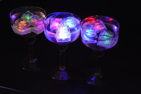 Plastic ice cubes with LEDs float in drinks of red, blue, green light. Stock Photos