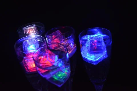 Plastic ice cubes with LEDs float in drinks of red, blue, green light. Stock Photos