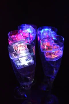 Plastic ice cubes with LEDs float in drinks of red, blue, green light. Stock Photos
