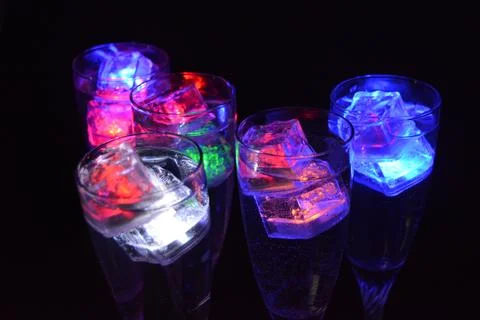 Plastic ice cubes with LEDs float in drinks of red, blue, green light. Stock Photos