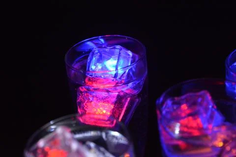 Plastic ice cubes with LEDs float in drinks of red, blue, green light. Stock Photos