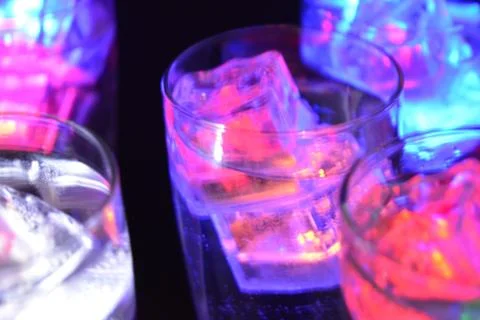 Plastic ice cubes with LEDs float in drinks of red, blue, green light. Foto stock