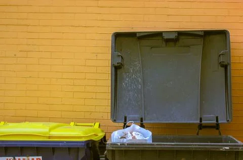 Plastic large trash cans with a lid up and garbage inside against a brick wall Stock Photos