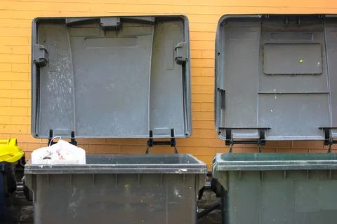 Plastic large trash cans with a lid up and garbage inside against a brick wall. Stock Photos
