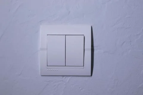 Plastic mechanical white light switch, installed on a light gray wall Stock Photos