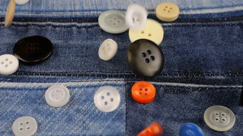 	Plastic multi-colored buttons fall on denim. Slow motion. Video stock 229486129