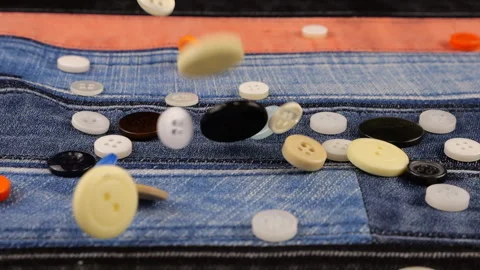 Plastic multi-colored buttons fall on denim. Slow motion. Video stock 229486427