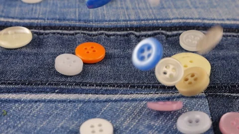 Plastic multi-colored buttons fall on denim. Slow motion. Video stock 229486476