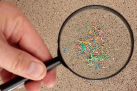 Plastic particles in the sand on the beach, under a magnifying glass. Foto stock