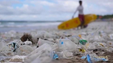Plastic pollution on beach and man with surfboard in background. Close-up of Stock Footage 257752041