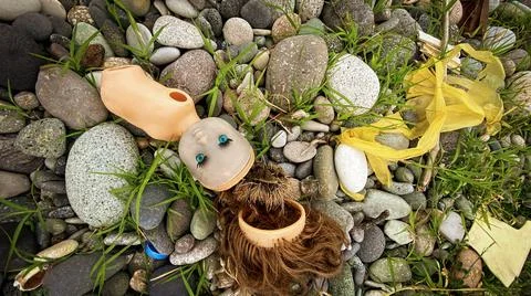 Plastic pollution: broken doll on a pebble beach Stockfoto's