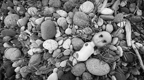Plastic pollution: broken doll on a pebble beach Fotos de archivo
