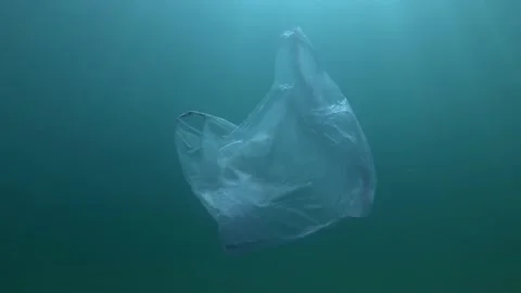 Plastic pollution, used blue plastic bag slowly drifting underwater in sunrays Stock Footage 133450154