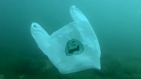 Plastic pollution, used white plastic bag with green smiley drifts underwater Stock Footage 129704206