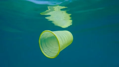 Plastic pollution, yellow plastic cup drifting underwater reflecting on the Stock Footage 140434450